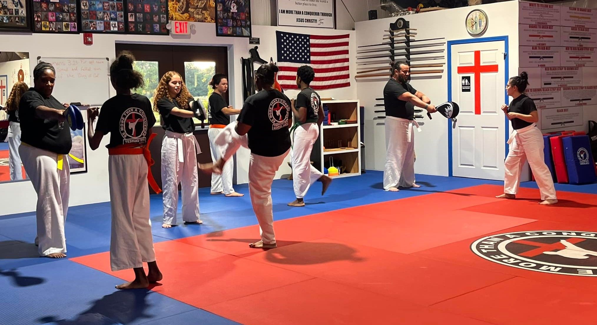 Students drilling kicks into pads held by partners across the dojo floor
