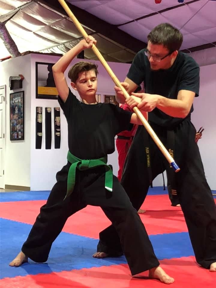 An instructor guiding a student's form with the bo staff
