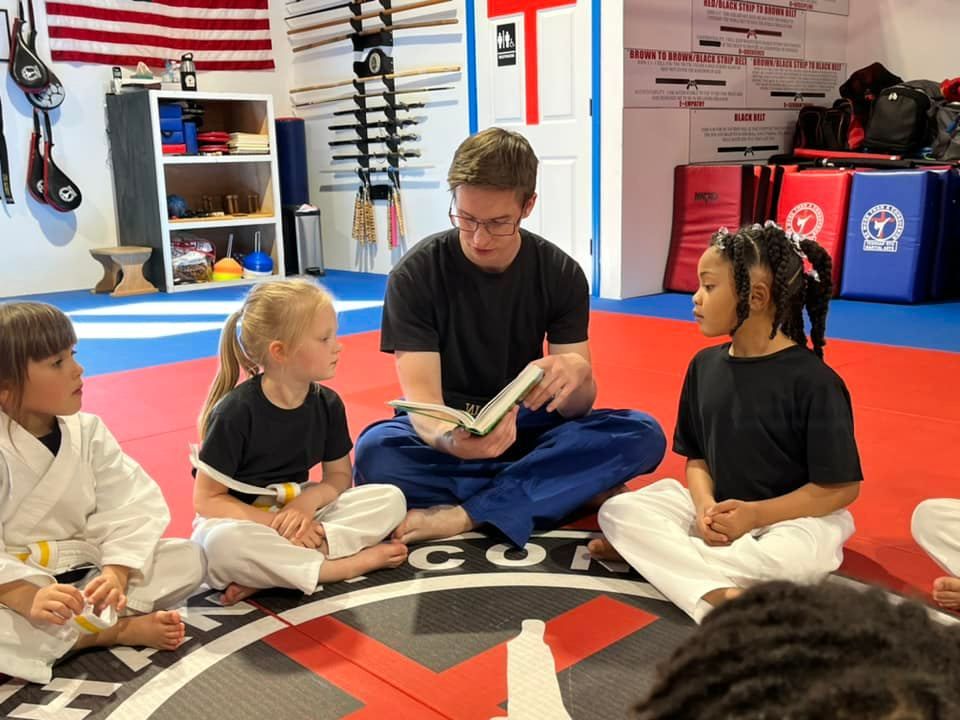 An instructor reading to a circle of students seated on the mat
