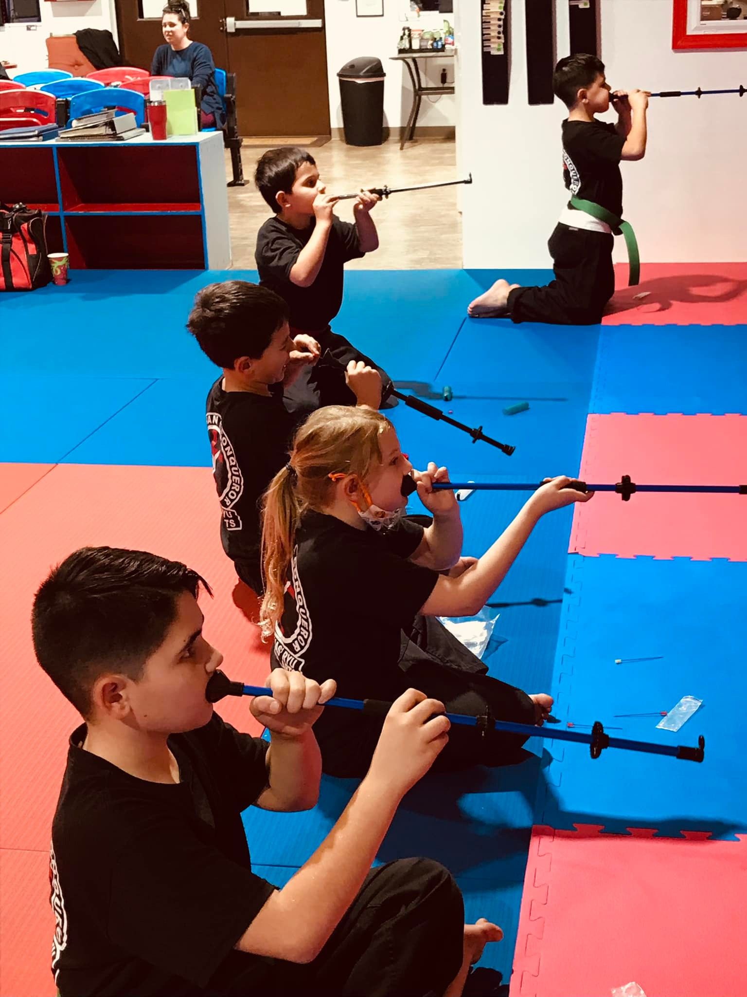 Kids kneeling in a line practicing blow darts at the throwing wall
